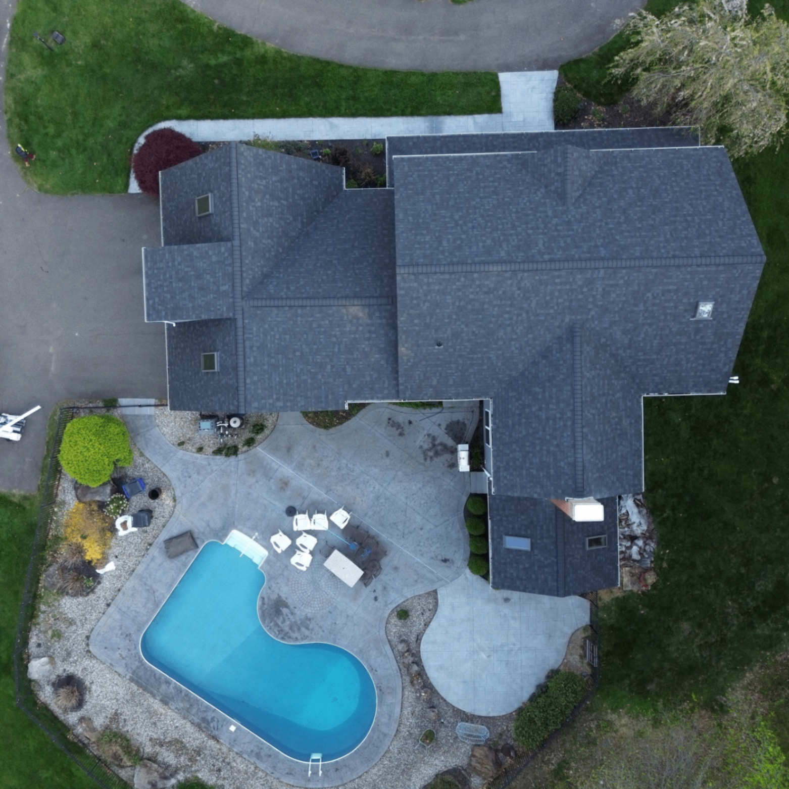 Top-down drone view of a completed dark shingle roof around a backyard pool.